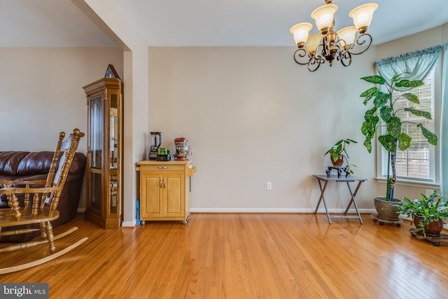 sitting room with light wood finished floors, plenty of natural light, baseboards, and an inviting chandelier