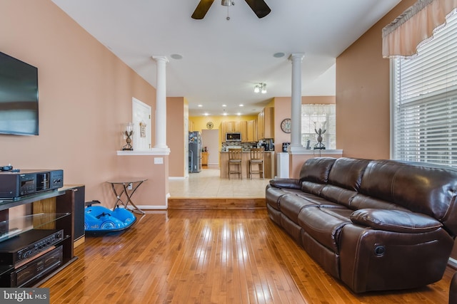 living room with baseboards, a ceiling fan, decorative columns, and light wood-style floors