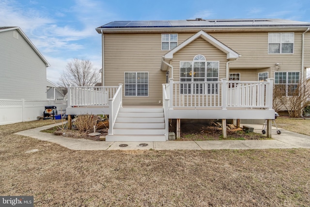 rear view of property with a deck, fence, stairs, and roof mounted solar panels