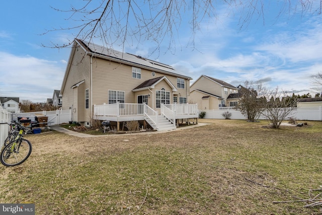 back of property featuring a deck, a lawn, a fenced backyard, and roof mounted solar panels