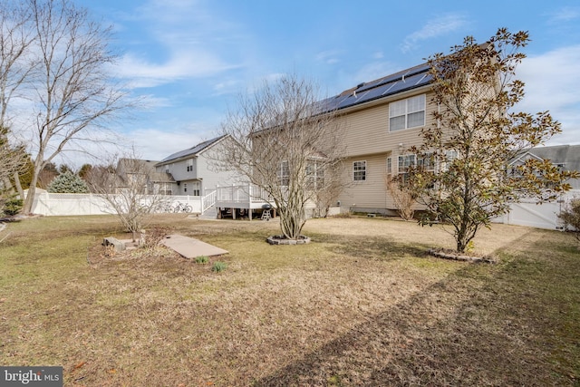 rear view of house featuring a lawn, fence, and solar panels