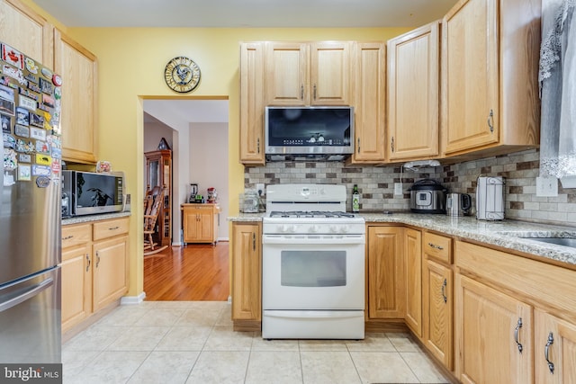 kitchen with light tile patterned floors, stainless steel appliances, decorative backsplash, and light brown cabinetry