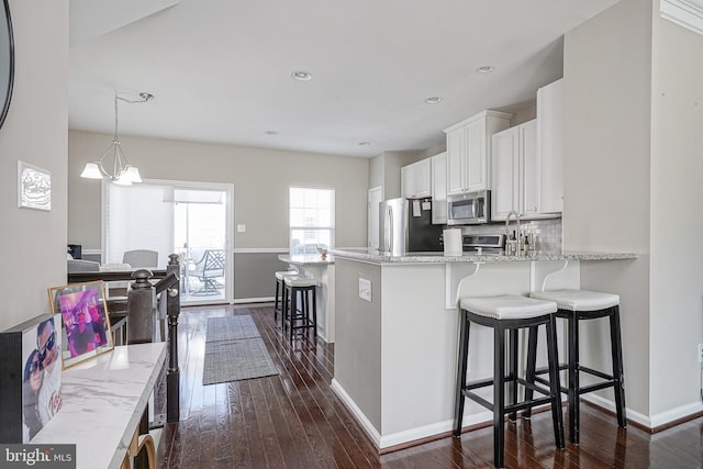 kitchen with dark wood-style floors, a breakfast bar, appliances with stainless steel finishes, white cabinetry, and backsplash