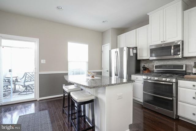 kitchen featuring dark wood-style floors, a center island, stainless steel appliances, white cabinets, and decorative backsplash