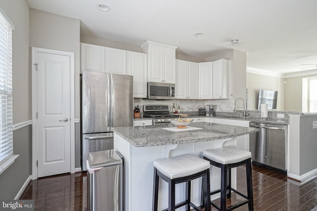 kitchen featuring a sink, a kitchen island, dark wood-style floors, stainless steel appliances, and a peninsula