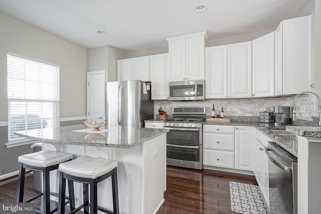 kitchen with a sink, a kitchen island, appliances with stainless steel finishes, decorative backsplash, and dark wood-style flooring