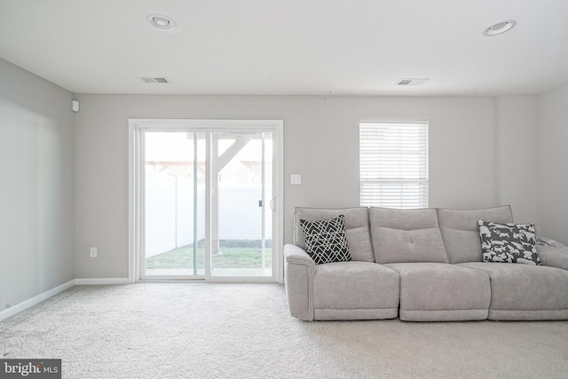 carpeted living area featuring a wealth of natural light, visible vents, and baseboards