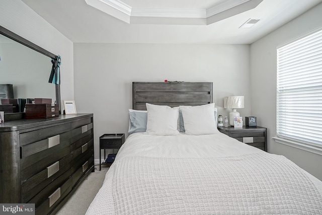 bedroom with a tray ceiling, light colored carpet, visible vents, and crown molding