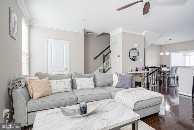 living area with a ceiling fan, dark wood-style floors, visible vents, ornamental molding, and stairs