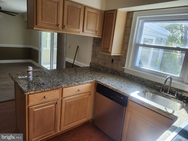 kitchen featuring a peninsula, dark wood-style flooring, a sink, dishwasher, and dark stone countertops