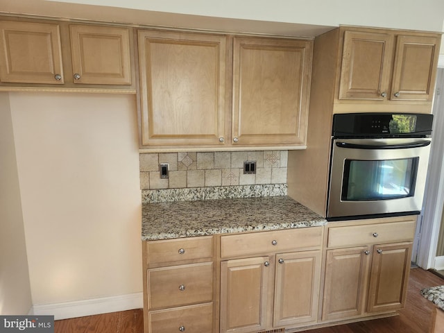 kitchen featuring light stone counters, dark wood finished floors, backsplash, light brown cabinetry, and stainless steel oven