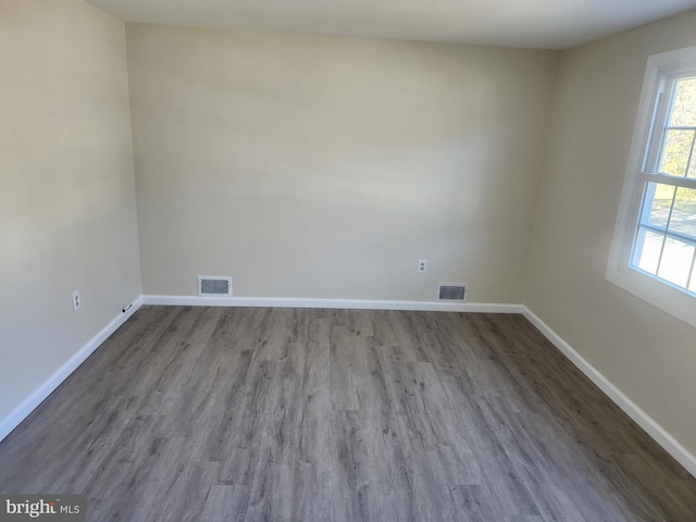 empty room with wood finished floors, visible vents, and baseboards