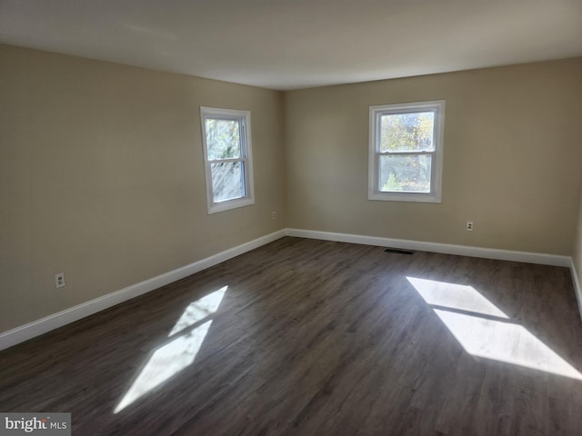 spare room featuring baseboards, dark wood-type flooring, and a wealth of natural light