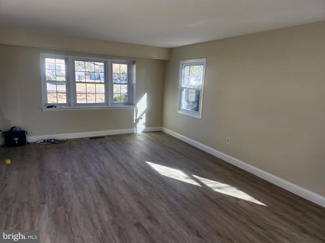 spare room featuring visible vents, baseboards, and dark wood finished floors