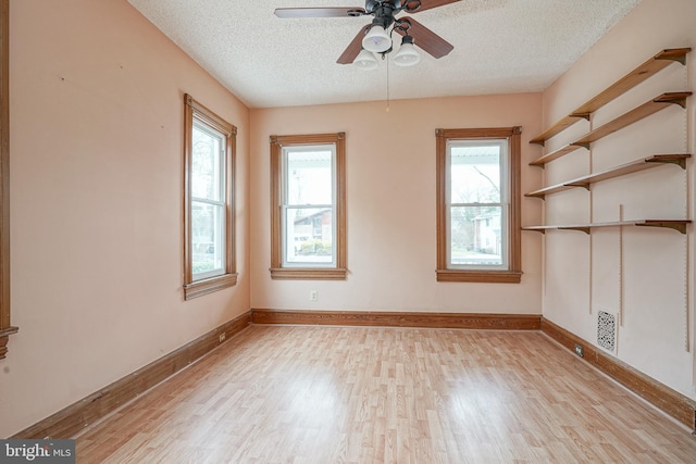 empty room with a healthy amount of sunlight, baseboards, light wood finished floors, and a textured ceiling