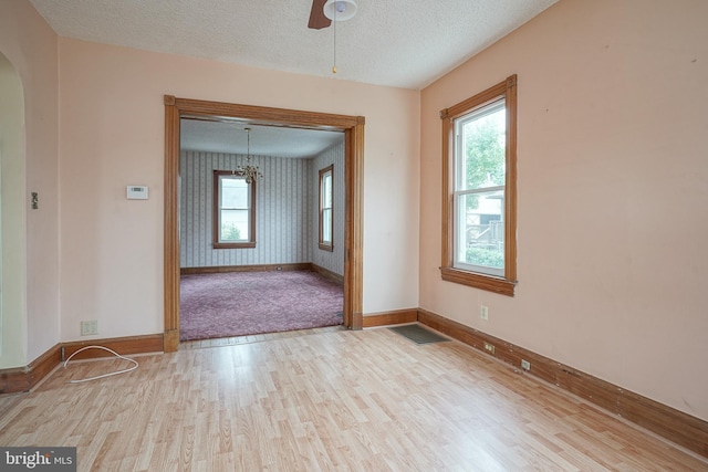 empty room with arched walkways, a textured ceiling, a healthy amount of sunlight, and wood finished floors