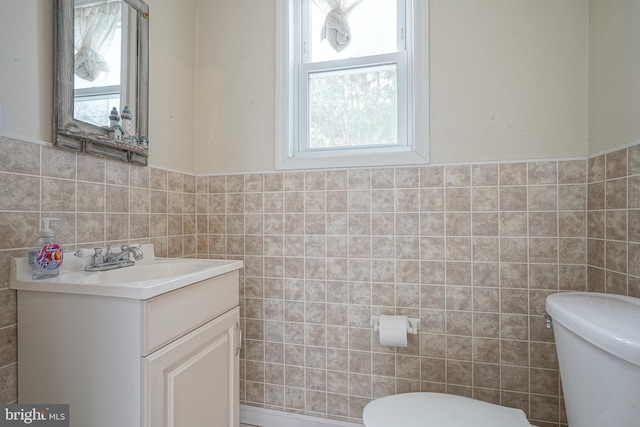 half bathroom featuring vanity, tile walls, toilet, and a wainscoted wall