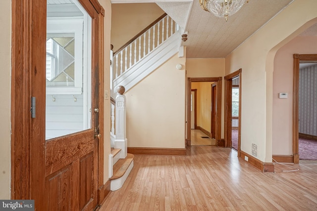 entryway with stairs, baseboards, arched walkways, and light wood finished floors