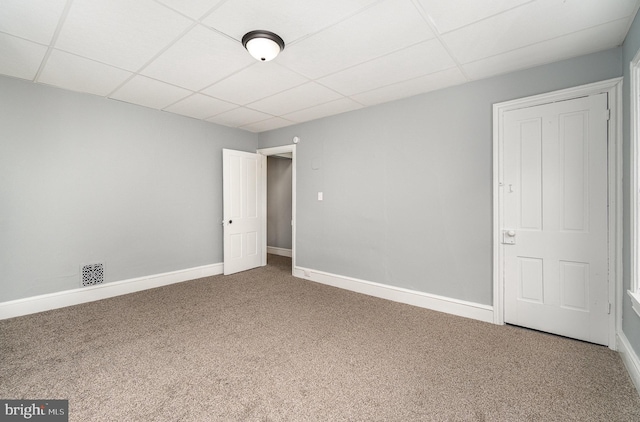 empty room featuring carpet floors, visible vents, baseboards, and a drop ceiling