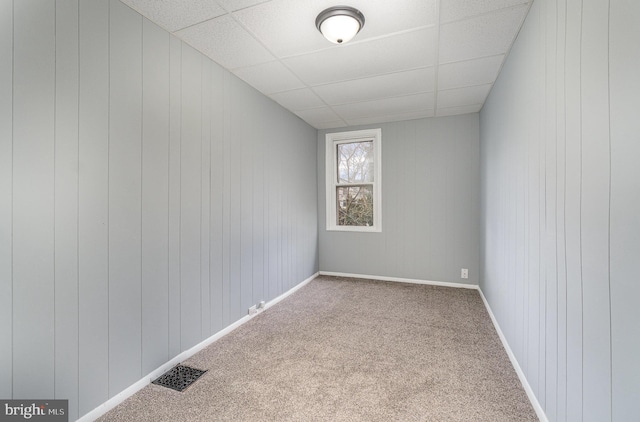 carpeted spare room with a paneled ceiling, baseboards, and visible vents