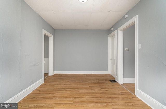 hallway with baseboards, a drop ceiling, visible vents, and light wood finished floors