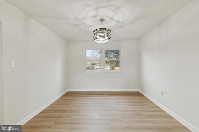 unfurnished dining area with baseboards, light wood finished floors, and an inviting chandelier