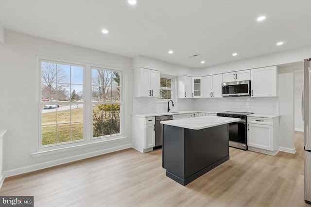 kitchen with appliances with stainless steel finishes, backsplash, light wood-type flooring, and a sink