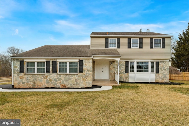 view of front of property with stone siding, a shingled roof, fence, and a front yard