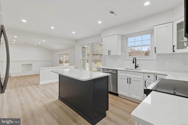 kitchen with lofted ceiling, light stone counters, a sink, stainless steel dishwasher, and light wood-type flooring