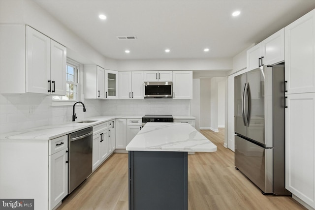 kitchen featuring light stone counters, stainless steel appliances, a kitchen island, a sink, and visible vents