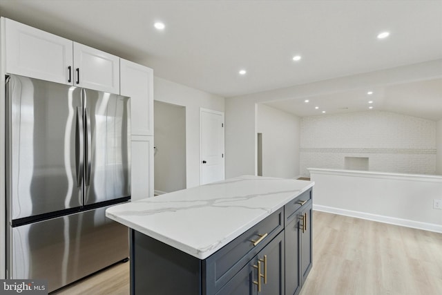 kitchen featuring light stone counters, freestanding refrigerator, white cabinets, a kitchen island, and light wood-type flooring