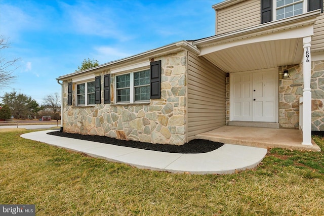 view of exterior entry with stone siding and a lawn