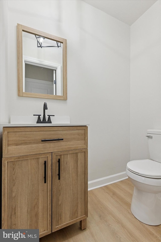 half bathroom featuring vanity, wood finished floors, toilet, and baseboards