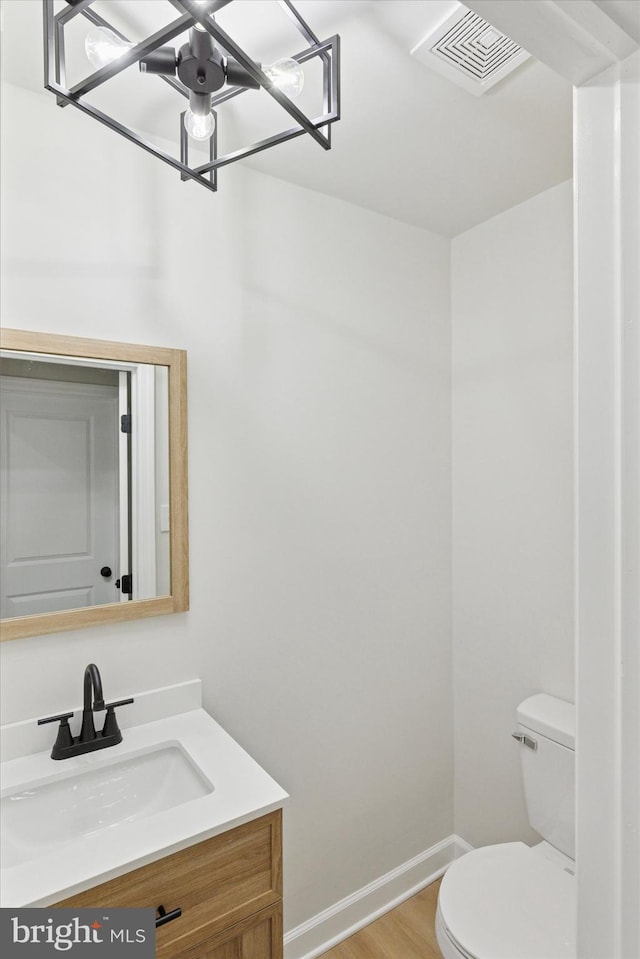 half bath with baseboards, visible vents, toilet, wood finished floors, and vanity