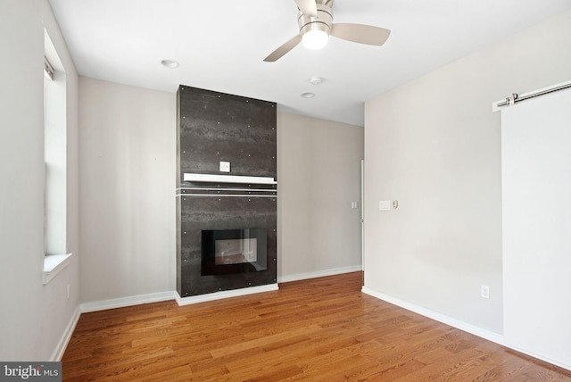 unfurnished living room with ceiling fan, a barn door, a fireplace, wood finished floors, and baseboards