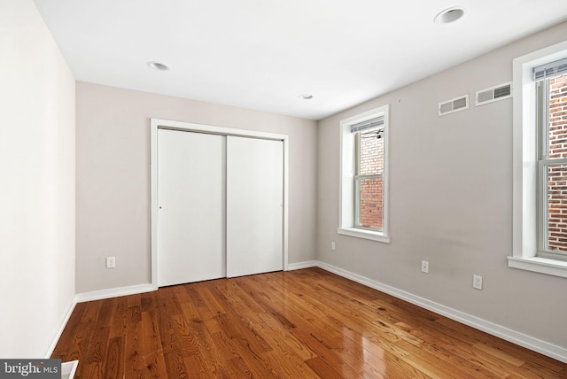 unfurnished bedroom with a closet, wood finished floors, visible vents, and baseboards