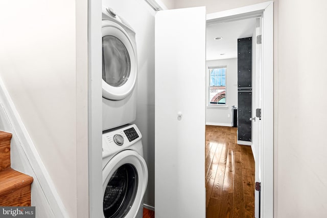 clothes washing area featuring stacked washer and clothes dryer, hardwood / wood-style flooring, baseboards, and laundry area