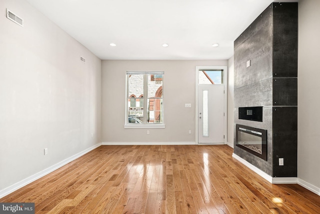 unfurnished living room featuring visible vents, light wood-style flooring, and baseboards