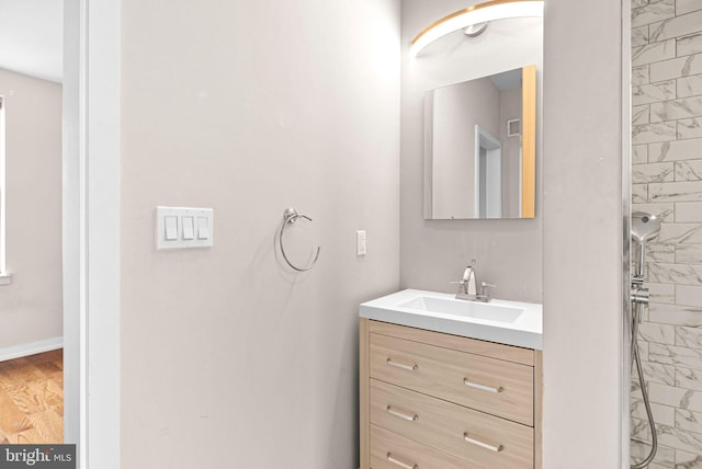 full bath featuring a tile shower, vanity, and baseboards