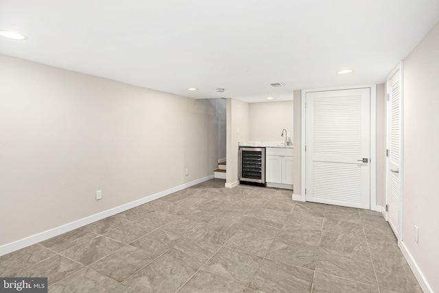 unfurnished living room featuring wine cooler, indoor wet bar, a sink, and baseboards