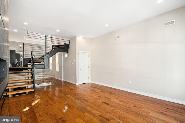 unfurnished living room featuring recessed lighting, visible vents, stairway, wood finished floors, and baseboards