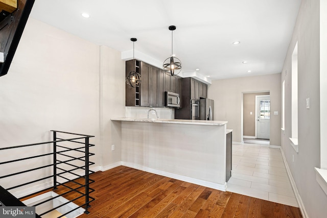 kitchen featuring pendant lighting, light wood-style flooring, decorative backsplash, appliances with stainless steel finishes, and a peninsula