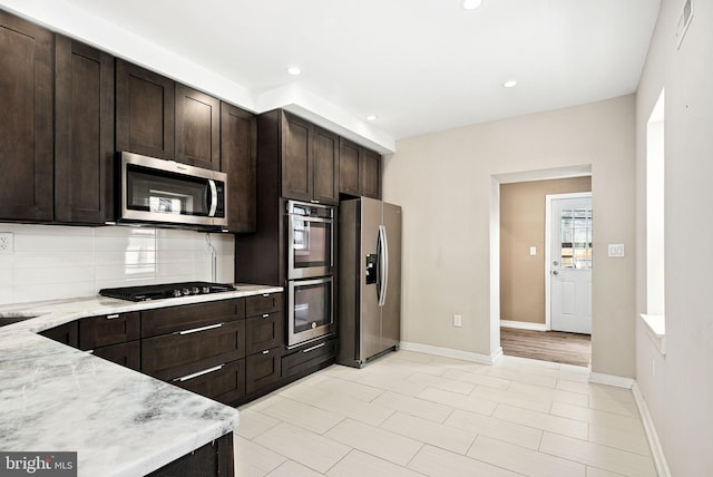 kitchen featuring baseboards, stainless steel appliances, dark brown cabinets, and decorative backsplash