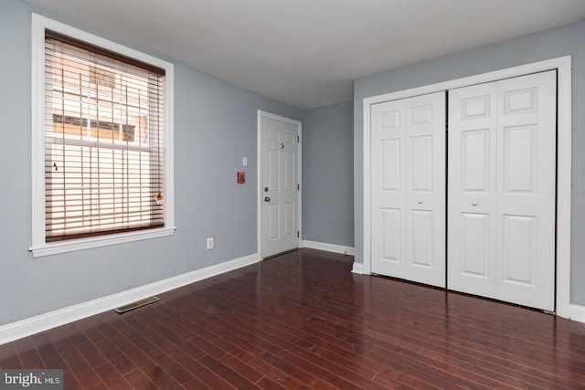 unfurnished bedroom featuring baseboards, a closet, visible vents, and wood finished floors