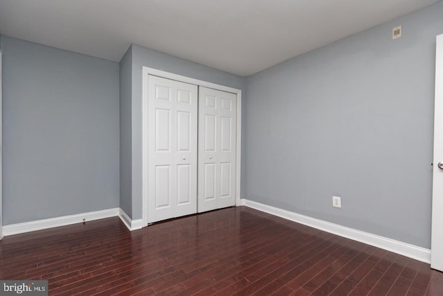 unfurnished bedroom with a closet, baseboards, and dark wood-style flooring