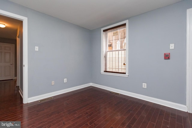 unfurnished room featuring dark wood-type flooring, visible vents, and baseboards