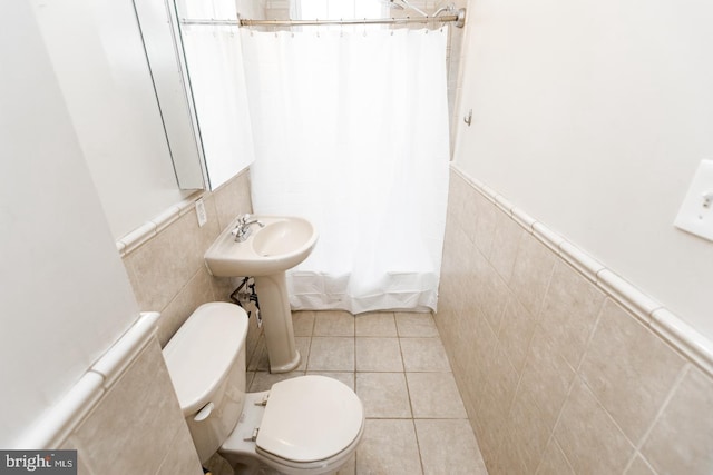 bathroom featuring toilet, tile patterned flooring, tile walls, and wainscoting