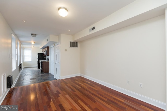 unfurnished room with dark wood-style flooring, visible vents, and baseboards