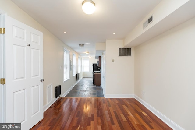 hallway with dark wood-style flooring, visible vents, and baseboards