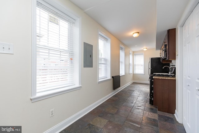 corridor with stone tile flooring, electric panel, and baseboards